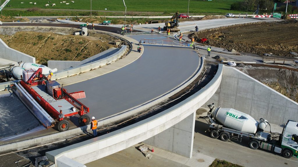 Coulage de la couche de roulage en béton armé continu sur l’anneau du pont giratoire de la Route de la Laine à Mouscron : machine de finition du béton et camion-malaxeur TRBA